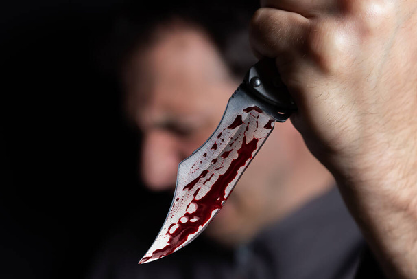 Knife with blood in the hand of a man. Threat with knife. Man attack with knife. Crime, violence. Selective focus. Blurred face - Foto, Imagen
