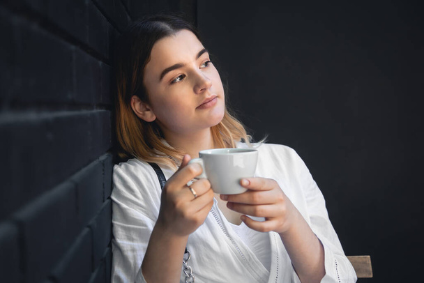 Młoda kobieta z filiżanką kawy we wnętrzu czarnej kawiarni pije drinka, kopiuje przestrzeń. - Zdjęcie, obraz
