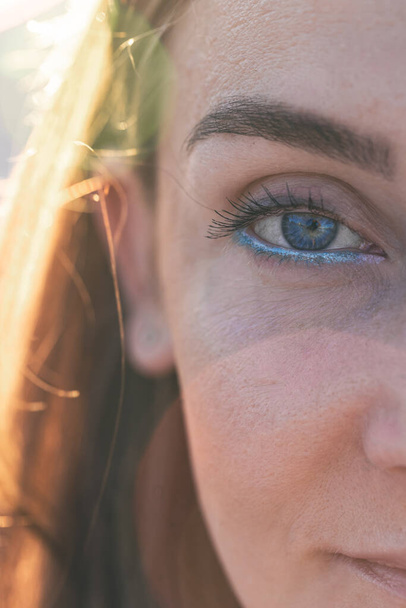 Портрет женщины на пляже с синей подводкой для глаз на размытом фоне на закате. - Фото, изображение
