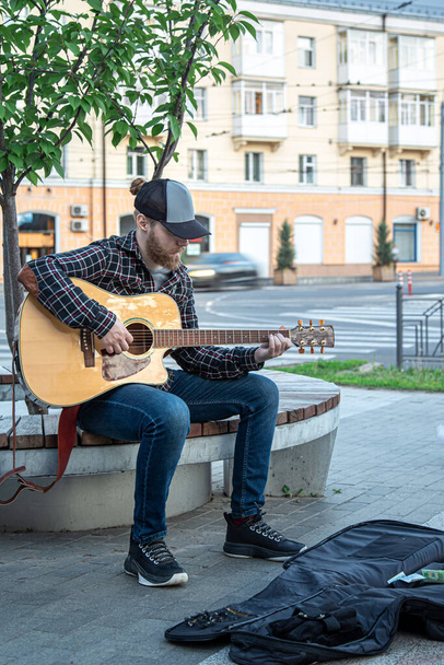 Muž pouliční hudebník s plnovousem a čepicí hraje na akustickou kytaru. - Fotografie, Obrázek
