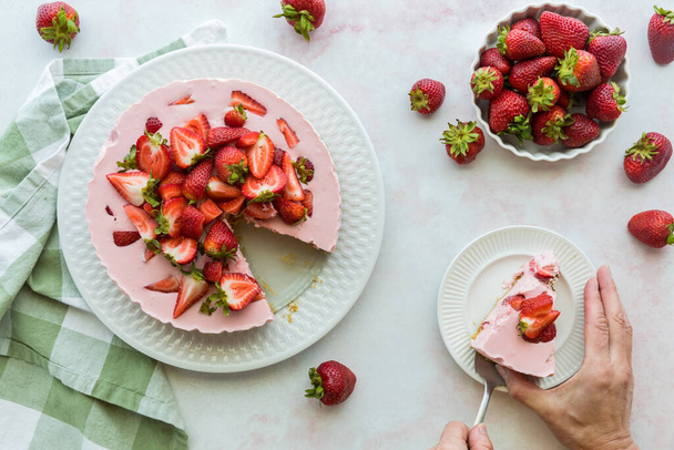 Ein schöner Erdbeer-Käsekuchen mit einer Scheibe, die zum Essen auf einen Teller gelegt wird. - Foto, Bild