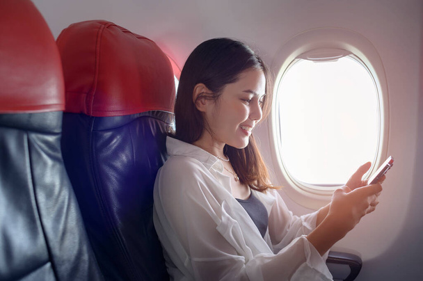A young beautiful woman is using smartphone on airplane, travel and holidays concept - Foto, Imagen