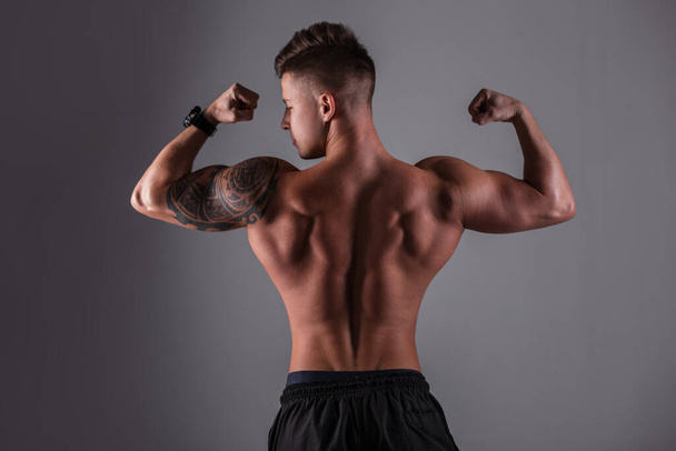 Sporty handsome bodybuilder guy with muscular rear and back poses and shows muscle against a dark background in the studio - Valokuva, kuva