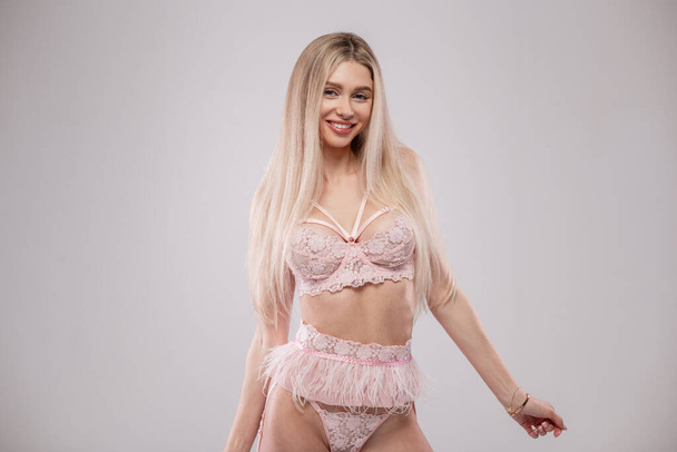 Hot blonde beautiful smiling happy woman with perfect sexy body in elegant pink lace lingerie poses on a gray background - Foto, imagen