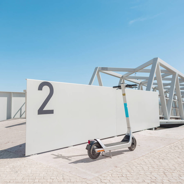 Elektroroller-Verleih steht in der Nähe der grauen Mauer in der Nähe der Seebrücke im sonnigen Portugal, Lissabon. Aktiver und gesunder Transport - Foto, Bild
