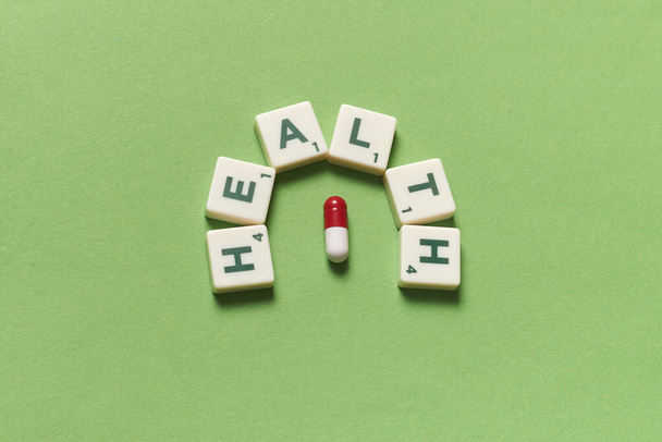 Health word formed of scrabble blocks and pharmaceutical pill over green background. Health and medical treatment concept. - Foto, imagen