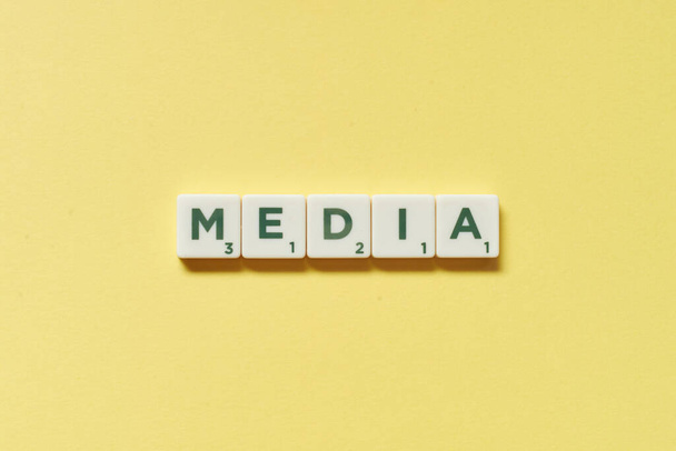 Media word formed of scrabble blocks on yellow background. Simple creative backdrop for business presentation. - Фото, зображення