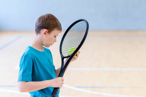 Trieste teleurgestelde jongen met tennis racket en bal in een lichamelijke opvoeding les - Foto, afbeelding