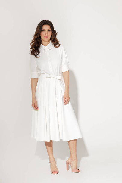 Self confident brunette women in white dress with wavy hair and natural fresh make-up posing on a white background. Spring or summer elegant fashion concept - Fotó, kép