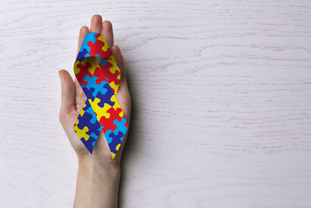 World Autism Awareness Day. Woman with colorful puzzle ribbon on white wooden background, top view with space for text - Valokuva, kuva