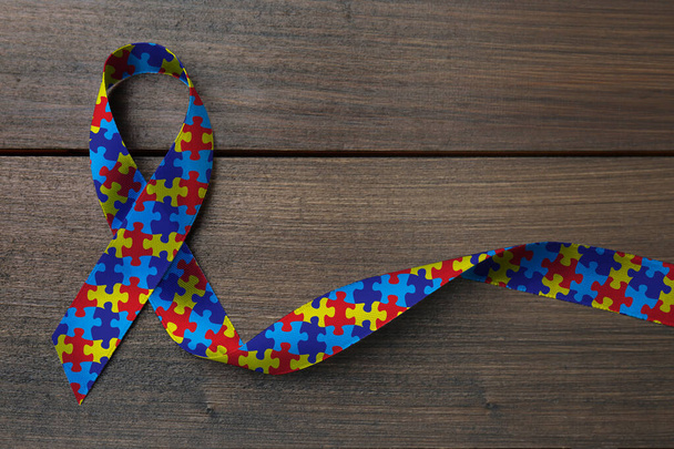 World Autism Awareness Day. Colorful puzzle ribbon on wooden background, top view - Foto, immagini