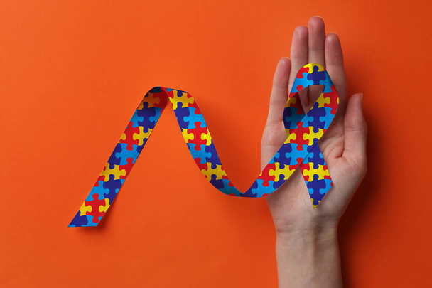 World Autism Awareness Day. Woman with colorful puzzle ribbon on orange background, top view - Photo, image