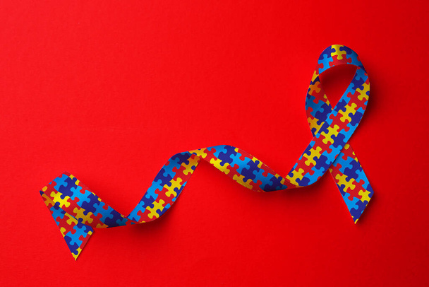 World Autism Awareness Day. Colorful puzzle ribbon on red background, top view - Photo, image