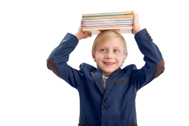 Mosolygó iskolás fiú portréja egy halom könyvvel a fején. Egy általános iskolás portréja. Fehér alapon elszigetelve - Fotó, kép