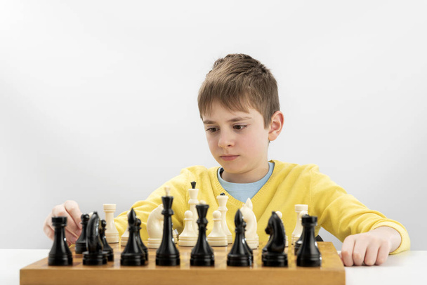 Portrait of child during chess game. Boy plays chess and thinks intently about the next move. Isolation on white background - Foto, imagen