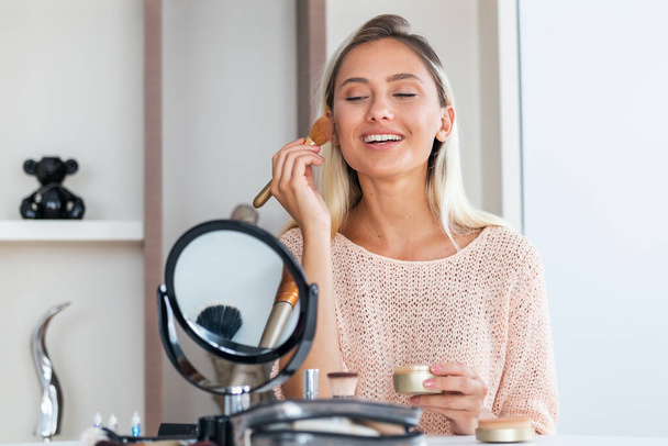 Mujer de belleza aplicando maquillaje. Hermosa chica mirándose en el espejo y aplicando cosméticos con un cepillo grande. La chica se sonroja en los pómulos. Polvo, colorete - Foto, imagen