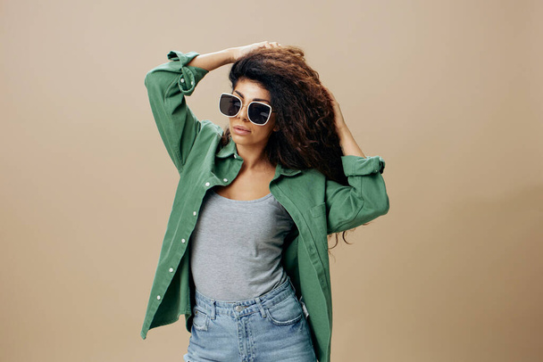 Fabulous pretty awesome tanned curly Latin female in casual things sunglasses touch hair posing isolated over pastel beige background look at camera. Copy space Mockup Banner. Fashion offer - Photo, Image