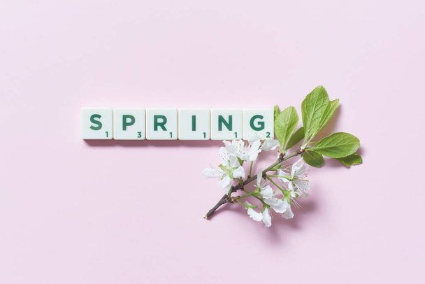 Wiosenne słowo utworzone z płytek scrabble ze świeżymi kwiatami drzewa na różowym tle. Oryginalny wzór kalendarza. - Zdjęcie, obraz