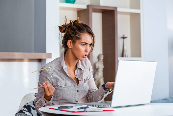 Młoda bizneswoman nieporozumienie jej laptop na biurku w biurze. kobieta pracująca z laptopem w domu lub nowoczesnym biurze. Poważny, zdezorientowany lub sfrustrowany wyraz twarzy. - Zdjęcie, obraz