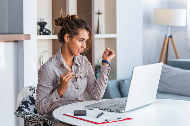 Молодая деловая женщина кусает очки и смотрит на свой ноутбук. - Фото, изображение