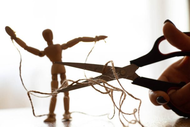 Houten marionet met touwen aan de poppenspeler vastgebonden en schaar sneed het touw door, manipulatie van mensen en vrijheid, kracht en vrijheid over macht - Foto, afbeelding