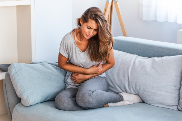 Woman lying on sofa looking sick in the living room. Beautiful young woman lying on bed and holding hands on her stomach. Woman having painful stomachache on bed, Menstrual period - Fotografie, Obrázek