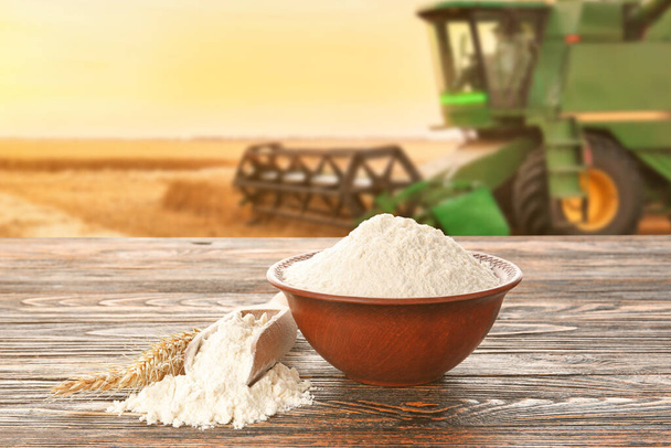 Cuenco con harina de trigo en la mesa de madera en el campo con cosechadora - Foto, Imagen