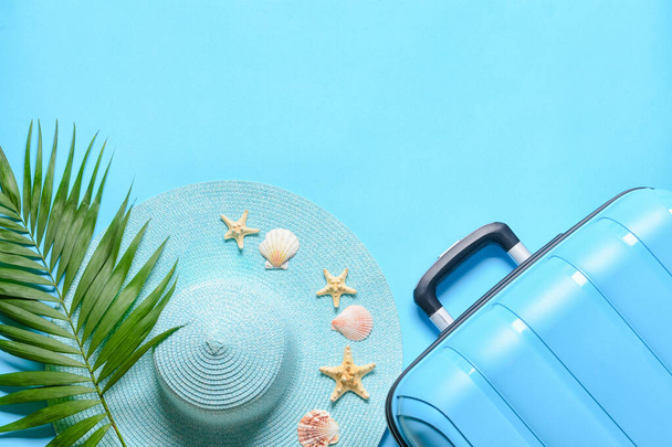 Suitcase, straw hat, palm leaf and seashells on blue background - Photo, Image
