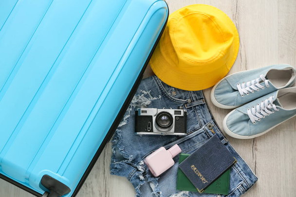 Blue suitcase, female clothes and traveler accessories on light wooden floor - Photo, image