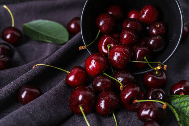 Overturned bowl of ripe cherries on fabric background, closeup - Фото, изображение
