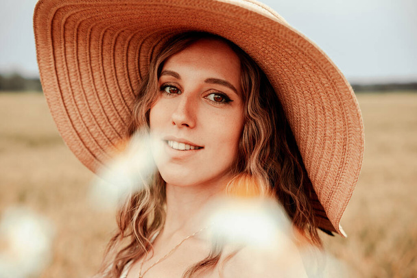 Buğday tarlası sahibi kadın. Güneş şapkalı mutlu genç kadın gün batımında buğday tarlasında. Doğa, yaz tatili, tarım ve insan konsepti - Fotoğraf, Görsel