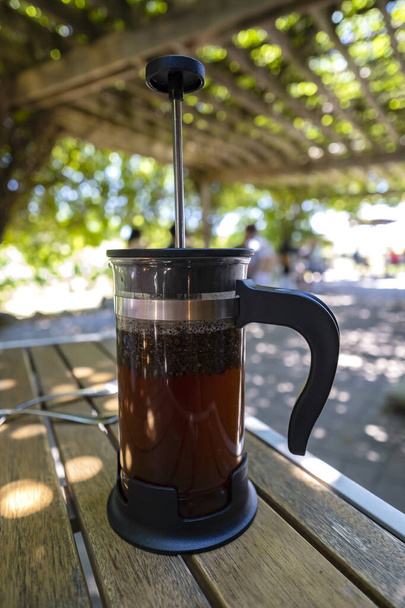 Small French Press Filled with Coffee Sitting on the Table of a Restaurant's Patio - Photo, Image