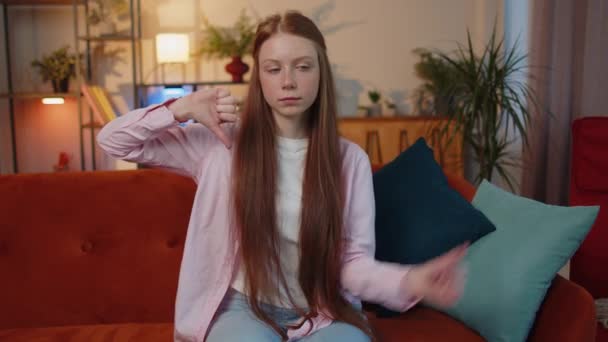 Dislike. Upset young teen child girl showing thumbs down sign gesture, expressing discontent, disapproval, dissatisfied bad work at modern home apartment indoor. Displeased kid in living room on sofa - Filmagem, Vídeo