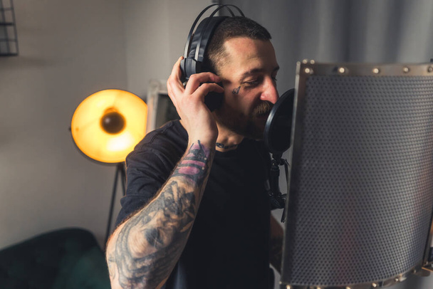 joven cantante tatuado graba música usando micrófono y auriculares espacio de copia plano medio. Foto de alta calidad - Foto, Imagen