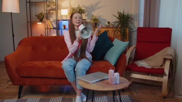 Junge rothaarige Teenagerin, die mit Megafon spricht, Nachrichten verkündet, lautstark Werbung ankündigt, über Lautsprecher davor warnt, im heimischen Wohnzimmer auf der Couch zu sprechen. Ingwerweibchen - Filmmaterial, Video