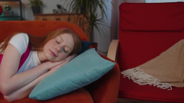 Tired one girl child lying down in bed taking a rest at home. Carefree young teen redhead children kid napping, falling asleep on comfortable sofa with pillows. Closed her eyes enjoy daytime nap alone - Footage, Video