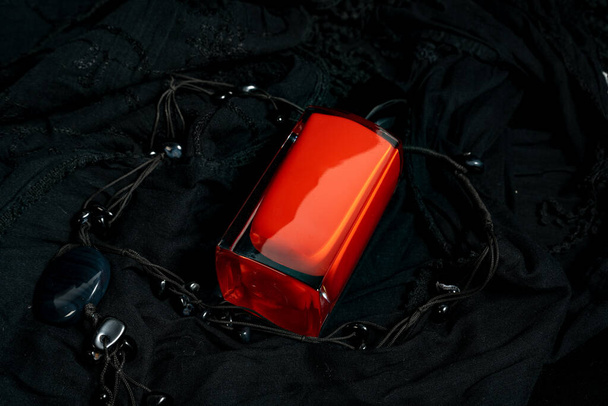close-up of a glass bottle of women's perfume. the bottle is red and is supported on a black background. it is in a horizontal position. There is also a pendant around the bottle - Photo, image