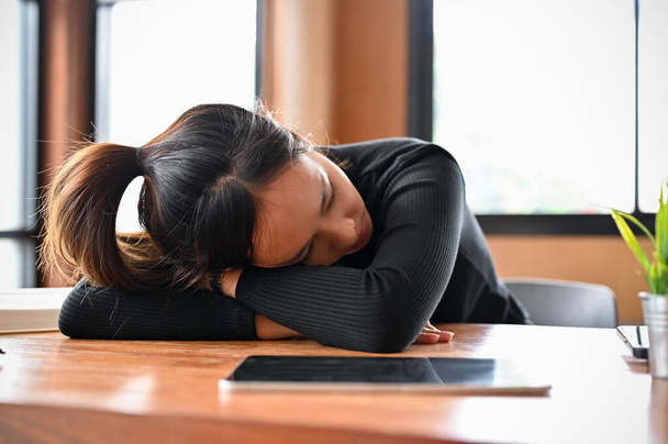 Moe slaperige jonge Aziatische vrouwelijke werknemer of student slapen op het bureau. Uitgeput door overbelasting. - Foto, afbeelding