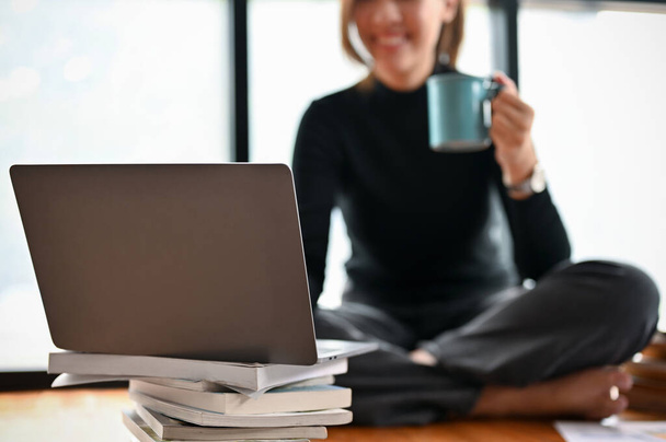 Escritora independiente que toma un café matutino mientras trabaja y usa una computadora portátil. imagen recortada y enfoque selectivo - Foto, Imagen