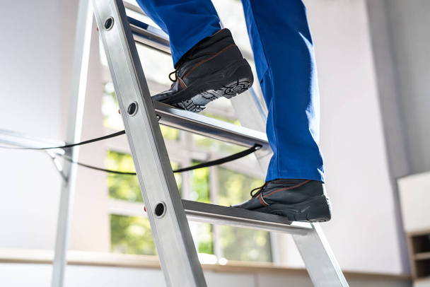 Low Section View Of A Handyman's Foot Climbing Ladder - 写真・画像