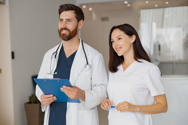Портрет врача и медсестры, стоящих у стойки регистрации в больнице и смотрящих в сторону. Высокое качество фото - Фото, изображение