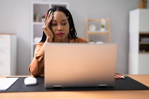 Стрессовая деловая женщина с помощью ноутбука, опираясь на стол в офисе - Фото, изображение
