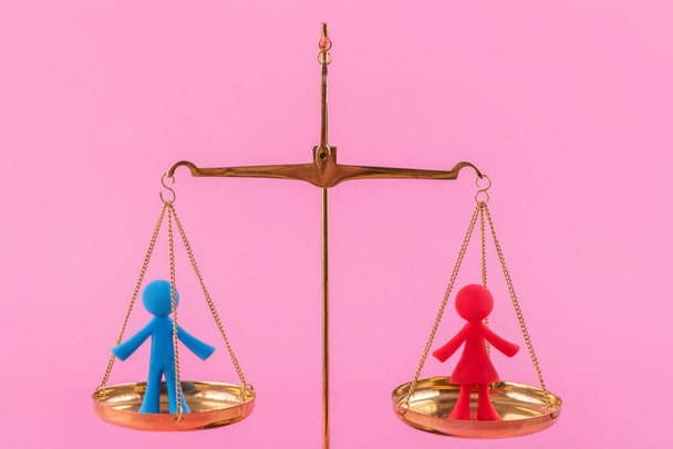 Symbolic figurines of a man and a woman on different scales on a pink background - Foto, Imagen