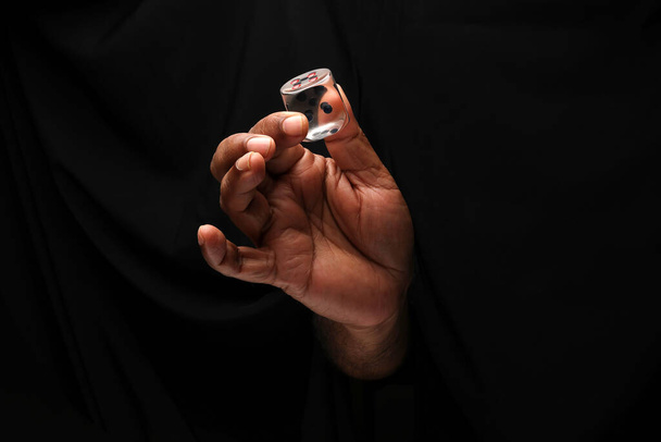 Asijské samec tmavé kůže jednou rukou pěst prst na černém pozadí drží transparentní akrylové plastové hrací kostky  - Fotografie, Obrázek