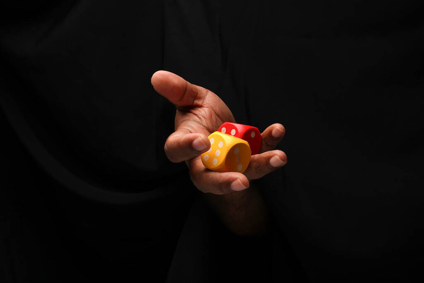 Asian male dark skinned single hand fist finger on black background holding wooden red yellow playing dice  - Photo, Image