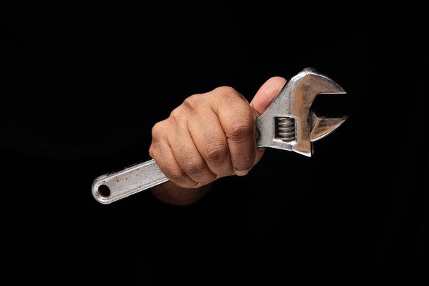 asiatico maschio scuro scuoiato singolo mano pugno dito su nero fondo holding utilizzando regolabile chiave inglese - Foto, immagini