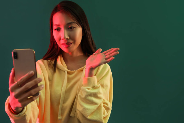 Female Asian blogger with smartphone on green background - Foto, Bild
