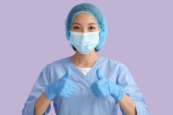 aziatische verpleegster in medisch masker tonen duim-up op kleur achtergrond - Foto, afbeelding