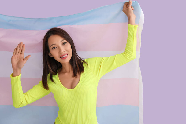Young Asian woman with transgender flag on lilac background - Photo, image