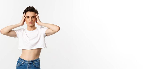 Lgbtq and pride concept. Beautiful and confident gay man wearing crop top, touching face and looking sassy at camera, standing over white background. - Fotó, kép